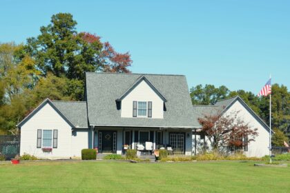 A light grey American family home with a front porch, a wide lawn and a US flag on a pole